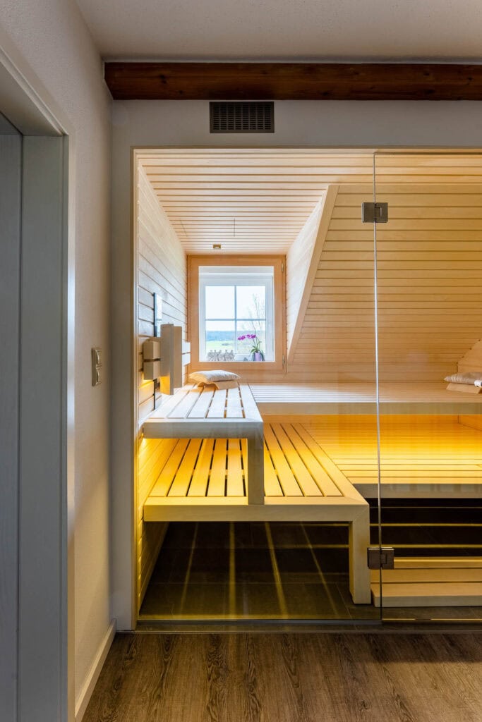 Sauna im Dachgeschoss unter dem sichtbaren Deckenbalken, Blick durch die Glasfront