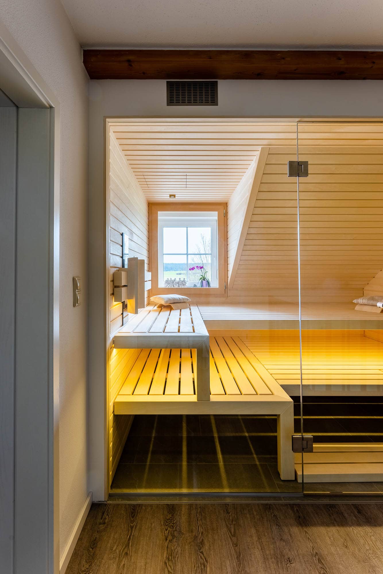 Sauna im Dachgeschoss unter dem sichtbaren Deckenbalken, Blick durch die Glasfront